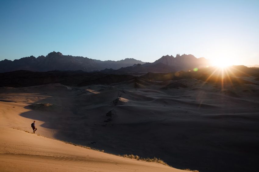 Travel - a person is walking in the desert at sunset