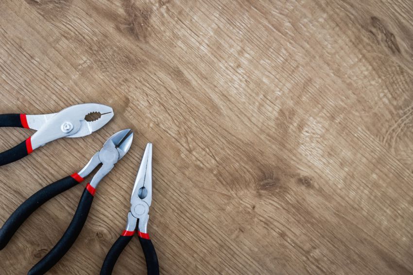 Tools - three black handled pliers on brown surface